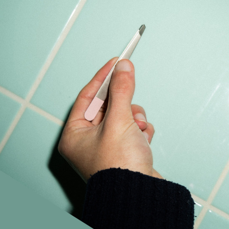 Un main qui tient la pince à épiler professionnelle avec mors bais.