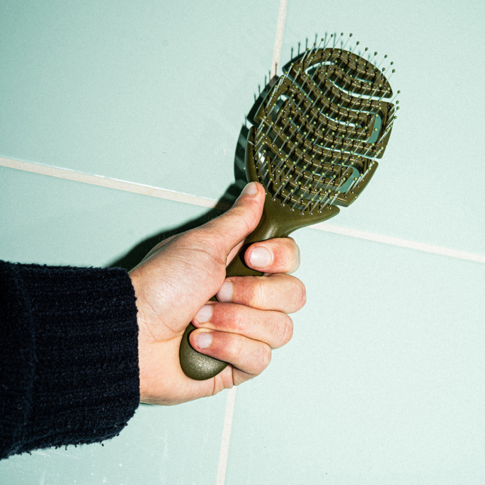 Un main qui tient notre brosse démêlante en kaki.