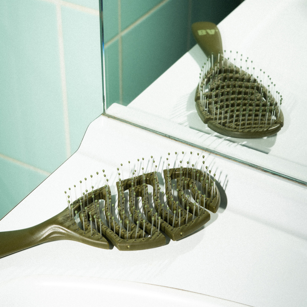 Notre brosse démêlante en kaki posée sur un lavabo.